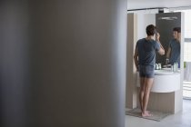 Молодой человек проверяет волосы в зеркале в ванной комнате — стоковое фото