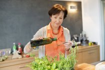 Mujer mayor vertiendo aceite de oliva en la cuchara en la cocina - foto de stock
