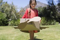 Маленькая девочка играет с картонным самолетом на газоне — стоковое фото