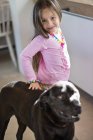 Portrait of smiling little girl standing with dog at home — Stock Photo