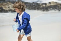 Усміхнений маленький хлопчик з кучерявим волоссям грає на пляжі — стокове фото