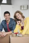 Lächelndes Paar beugt sich in Wohnung über Pappkartons und blickt in Kamera — Stockfoto