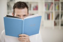 Portrait of playful man holding book in front of face — Stock Photo