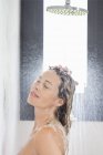 Donna rilassata con gli occhi chiusi facendo la doccia in bagno — Foto stock