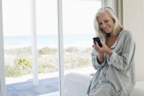 Усміхнена жінка використовує мобільний телефон у прибережному будинку — стокове фото
