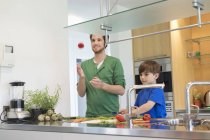 Homem e filho cortando legumes na cozinha moderna — Fotografia de Stock