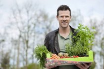 Portrait of man holding tray of raw vegetables outdoors — Stock Photo