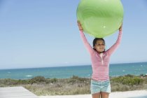 Усміхнена маленька дівчинка тримає фітнес-кулю на пляжі — стокове фото