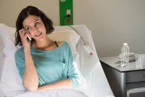 Жінка-пацієнтка розмовляє на мобільному телефоні на ліжку в лікарні — стокове фото