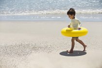 Niño pequeño caminando con anillo inflable en la playa de verano - foto de stock