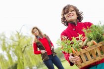 Menino segurando uma caixa de legumes variados com sua mãe em uma fazenda — Fotografia de Stock