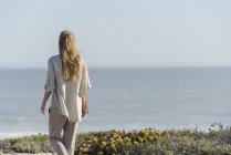 Вид ззаду жінки, що стоїть на пляжі і дивиться на вигляд — стокове фото