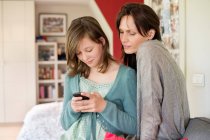 Messagerie texte fille sur téléphone mobile avec sa mère à la maison — Photo de stock