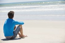 Homme rêveur assis sur la plage de sable et regardant la vue — Photo de stock