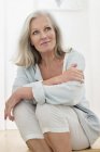 Dreamy senior woman sitting on floor at home and looking away — Stock Photo