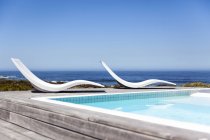 Moderne Liegestühle am Pool an der Küste unter klarem Himmel — Stockfoto