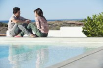 Romantic couple sitting at poolside on beach and talking — Stock Photo