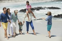Мальчик фотографирует семью, гуляющую по песчаному пляжу — стоковое фото