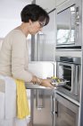 Senior woman putting tray of seafood into oven in kitchen — Stock Photo