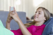 Lächelndes Teenie-Mädchen auf Sitzsack liegend und mit Handy — Stockfoto
