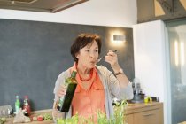 Senior woman tasting olive oil in kitchen — Stock Photo