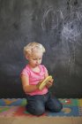 Cute little girl playing with number puzzle in front of a blackboard — Stock Photo