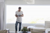 Junger schöner Mann liest Magazin im Wohnzimmer zu Hause — Stockfoto