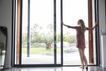 Frau steht am Glasfenster mit Gartenblick — Stockfoto