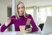 Geschäftsfrau isst Salat, während sie Handy benutzt — Stockfoto