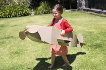 Bambina che gioca con l'aereo di cartone sul prato — Foto stock