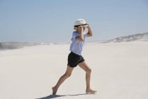 Девушка в шляпе идет по солнечному песчаному пляжу — стоковое фото