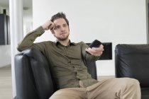 Positive young man watching television on sofa at home — Stock Photo