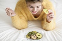 Женщина в желтом пушистом свитере ест печенье на кровати — стоковое фото