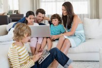 Хлопчик використовує цифровий планшет зі своєю родиною, дивлячись на ноутбук — стокове фото