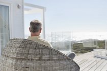 Чоловік розслабляється в плетеному кріслі на терасі будинку на морському узбережжі — стокове фото