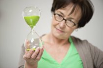 Senior woman looking at hourglass on grey background — Stock Photo