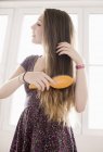 Teenage girl brushing hair in front of window — Stock Photo