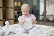 Cute baby girl playing with tambourine on bed at home — Stock Photo
