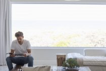Junger Mann liest zu Hause im Wohnzimmer Magazin — Stockfoto