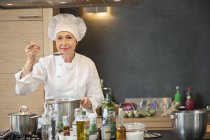 Woman in chef costume tasting food in kitchen — Stock Photo