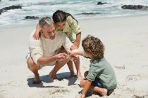 Niños con su abuelo en la playa - foto de stock