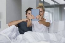 Jeune couple prenant selfie avec tablette numérique sur le lit — Photo de stock
