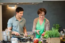 Mulher ajudando seu filho a cozinhar comida na cozinha — Fotografia de Stock