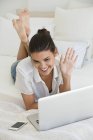 Woman having online video chat with laptop while lying on bed — Stock Photo