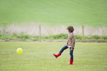 Мальчик играет с мячом на зеленом осеннем поле — стоковое фото