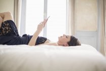Елегантна жінка лежить на ліжку і використовує мобільний телефон — стокове фото