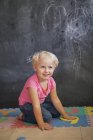 Lächelndes süßes kleines Mädchen, das vor einer Tafel mit Zahlenrätsel spielt — Stockfoto