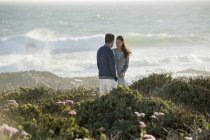 Couple standing in vegetation on sea coast and looking at each other — Stock Photo