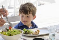 Счастливый маленький мальчик обедает за столом — стоковое фото
