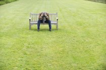 Depressed man sitting on wooden bench in green field — Stock Photo